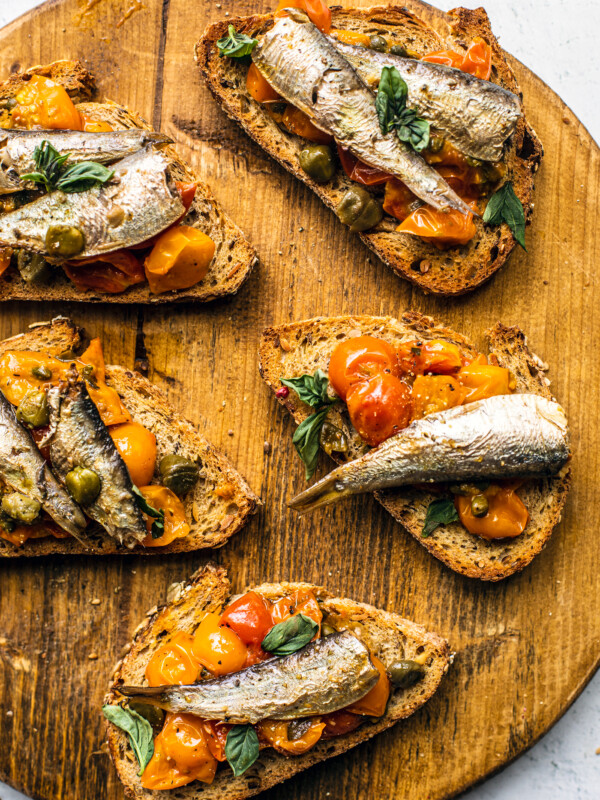 Wooden serving board with toasts topped with tomato confit and sardines.