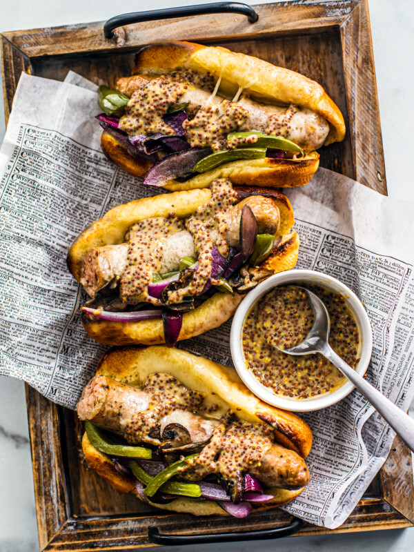 Three buns stuffed with sausage and peppers on a tray with a small bowl of mustard