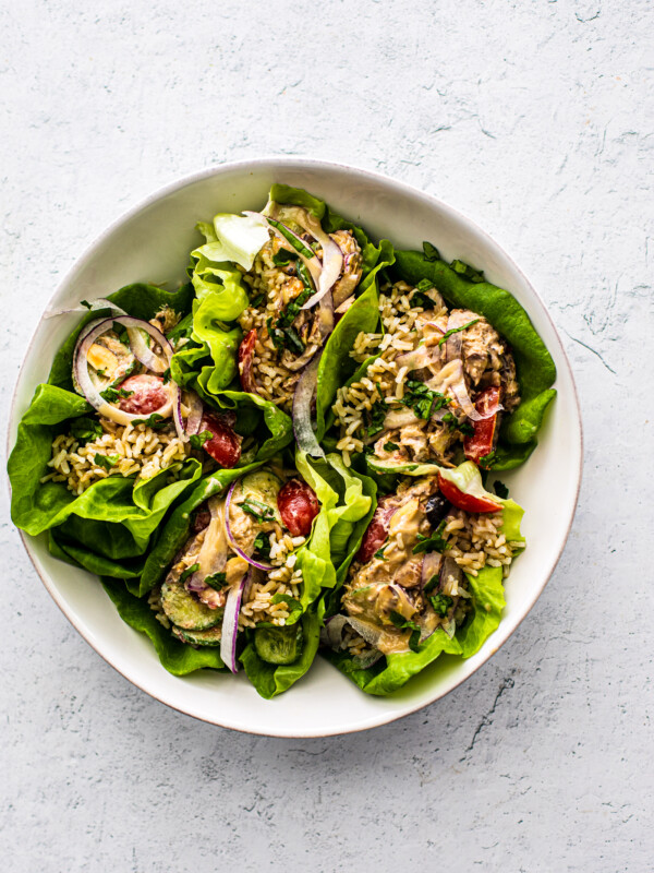 Lettuce wraps stuffed with rice and mackerel propped into a white serving bowl.