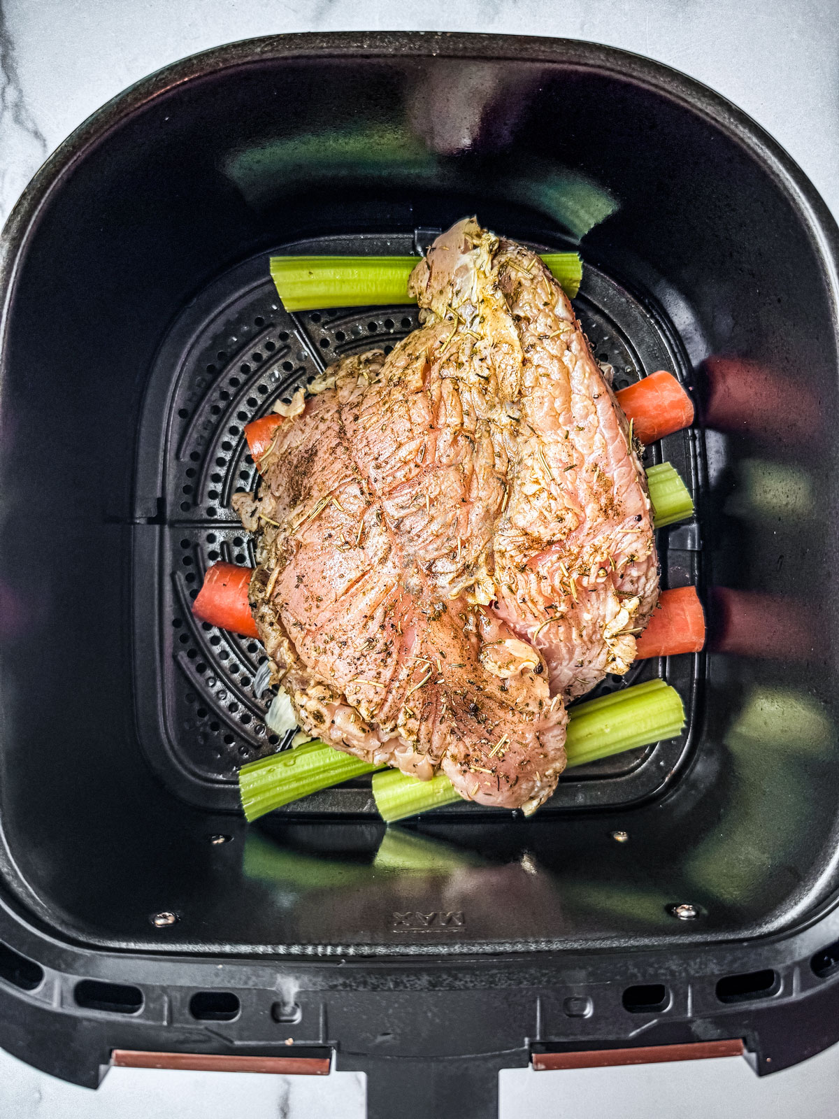 Seasoned turkey breast, uncooked, placed in the air fryer basket.