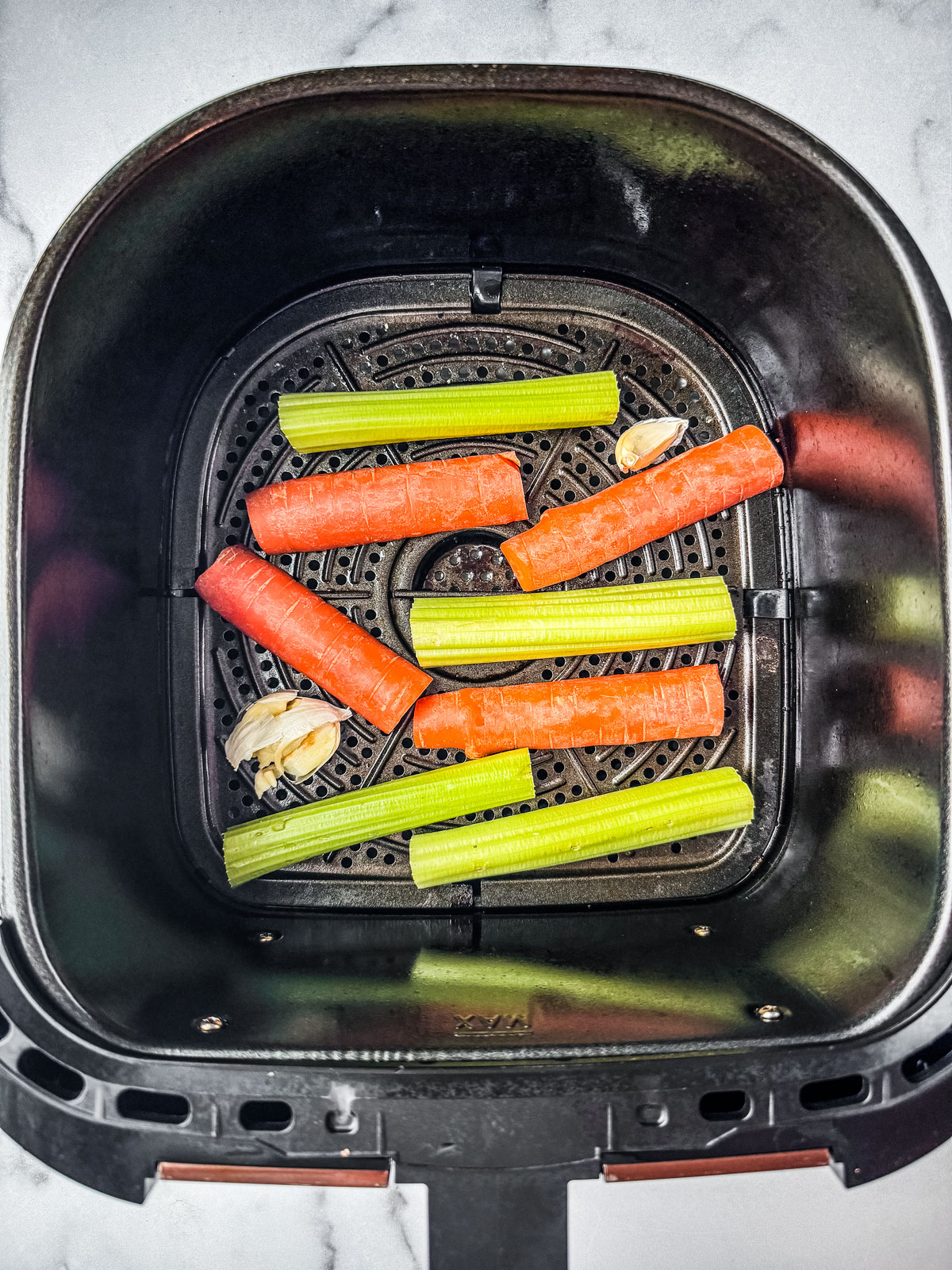 Carrots and celery lining the basket of an air fryer.