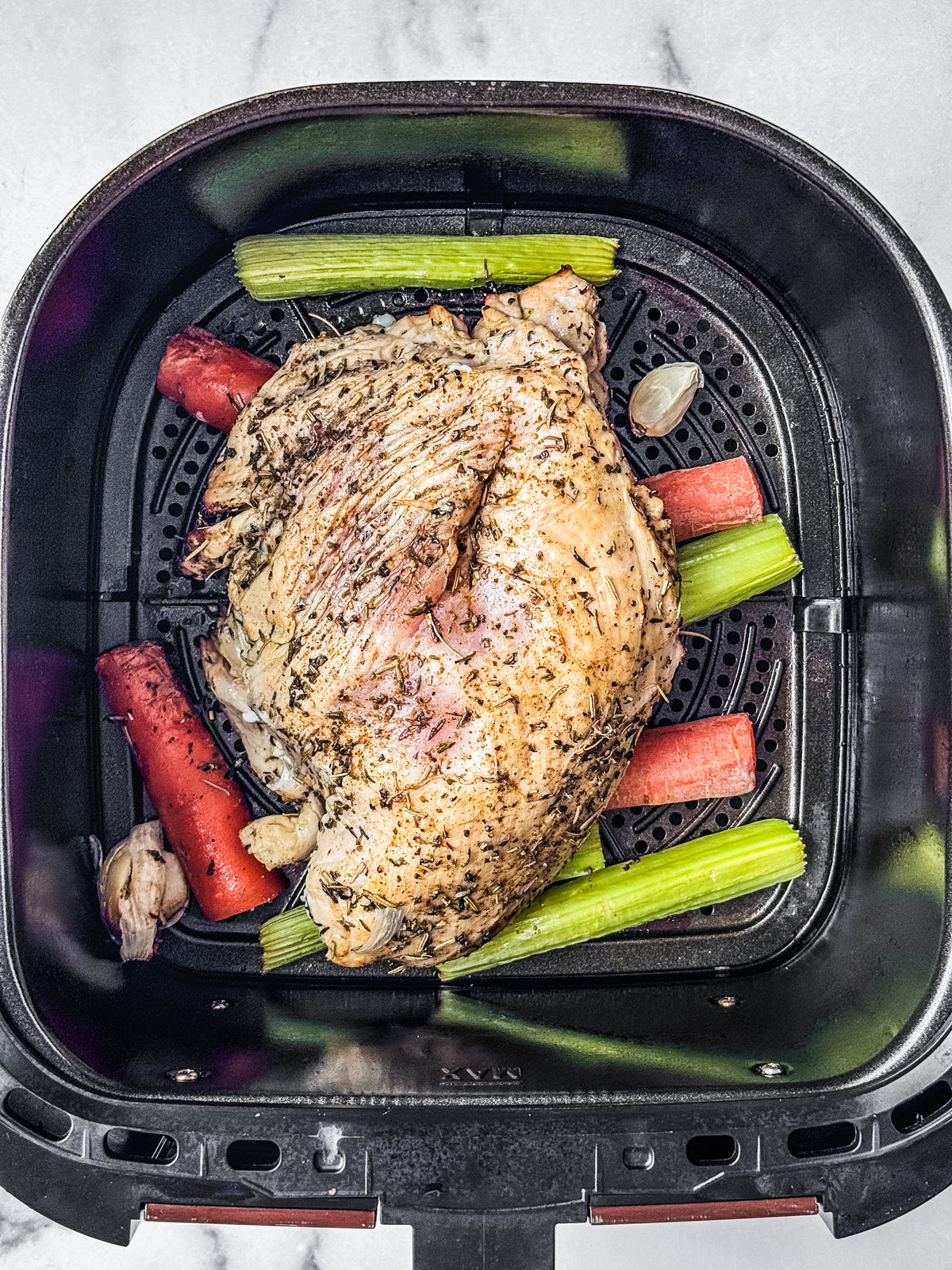 Half cooked turkey flipped over in the air fryer basket.