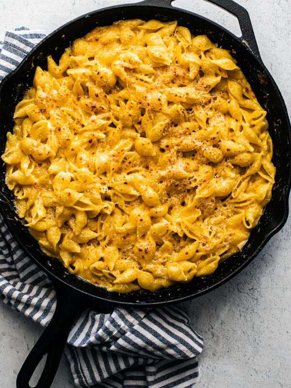 Baked mac and cheese in a cast iron skillet with a kitchen towel wrapped around part of it.