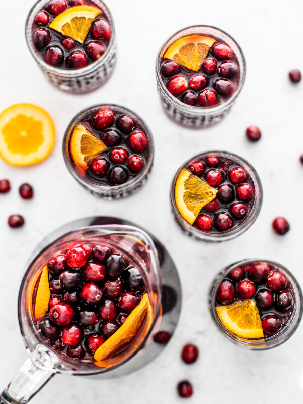 Overhead shot of pitcher and cocktail glasses full of sangria, cranberries, and oranges.