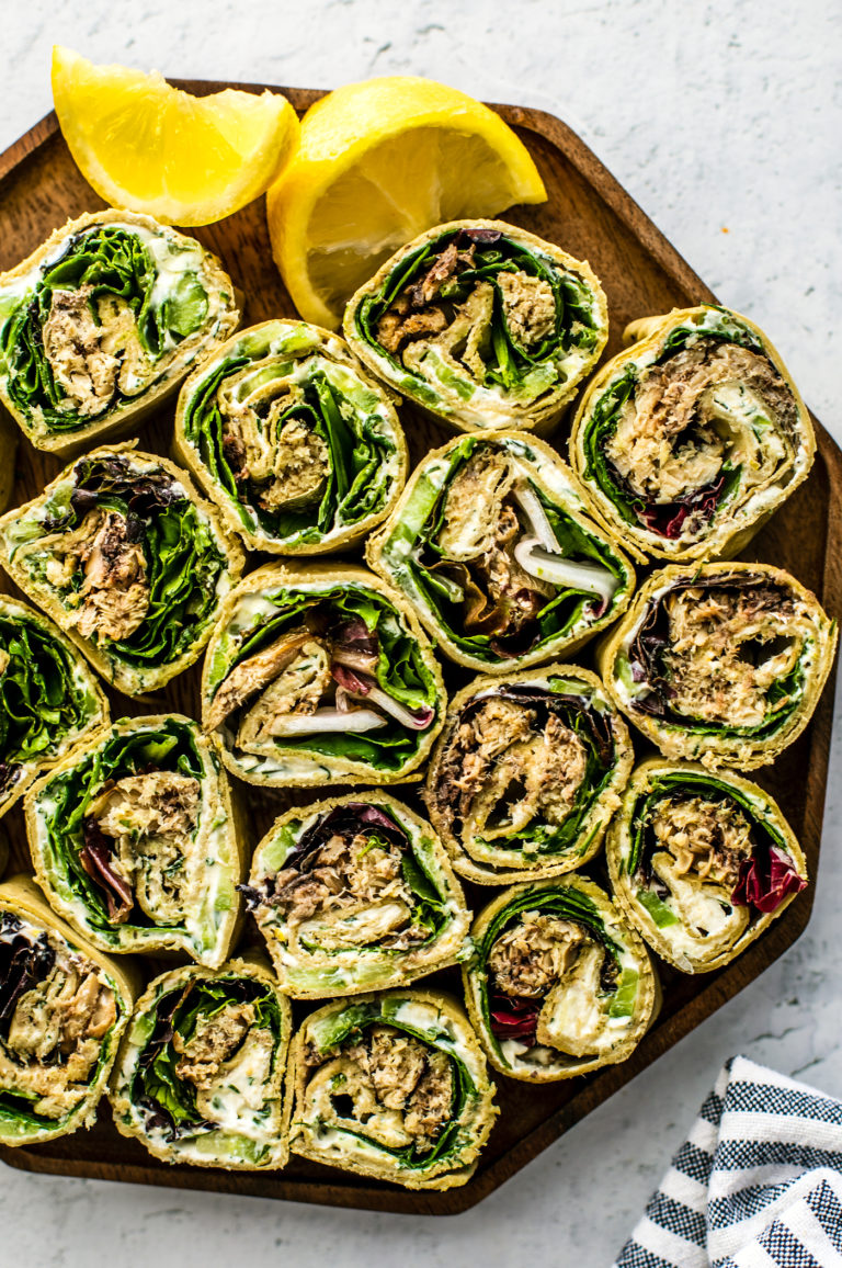 Pinwheel sandwiches on a wooden serving plate with lemon wedges on the side.