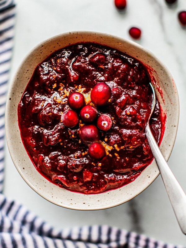 Speckled serving bowl full of cranberry sauce, topped with orange zest and fresh cranberries.