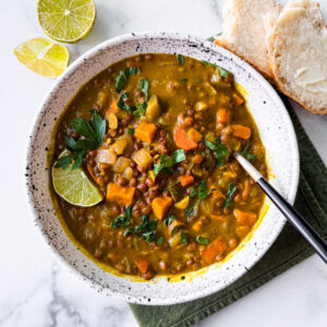 Bowl of Instant Pot lentil soup with a side of bread and lime wedges.