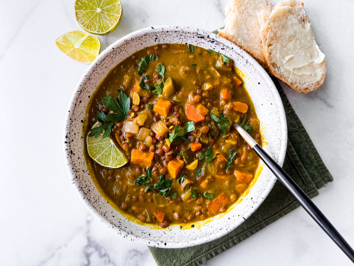 Bowl of Instant Pot lentil soup with a side of bread and lime wedges.