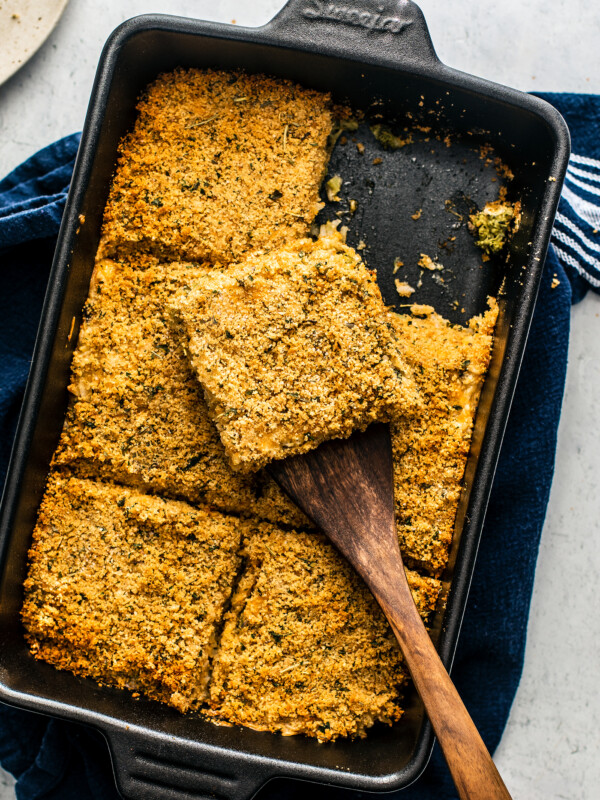 Cast iron casserole dish of broccoli casserole with a spatula scooping a portion.