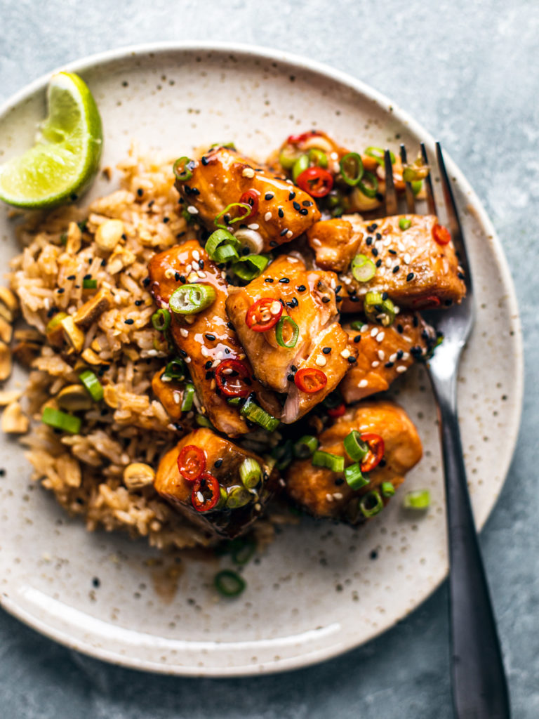 Plate with rice topped with cubed salmon tossed in sweet chili sauce and garnished with scallions and chilies.