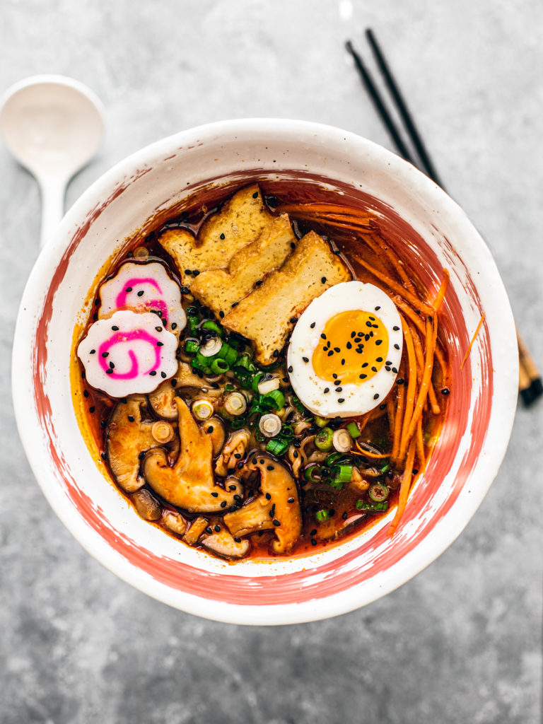 Bowl of shoyu ramen with mushrooms, scallions, narutomaki, egg, and carrots.