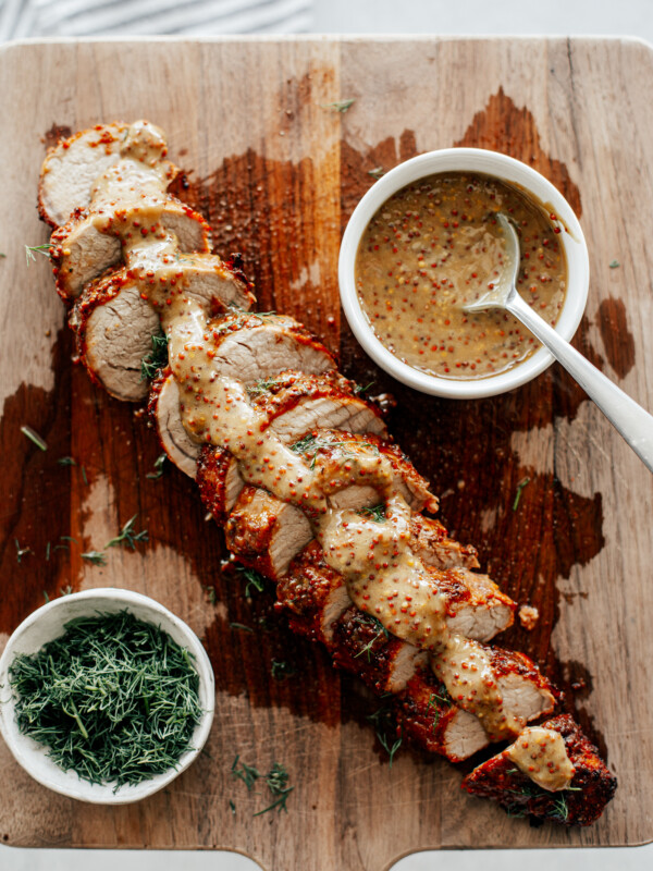 Sliced pork tenderloin on a wooden board drizzled with mustard sauce.