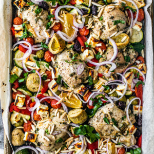 Seasoned chicken thighs on a sheet pan with vegetables and crumbled feta.