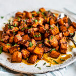 Close up side shot of serving plate full of honey lime sweet potatoes garnished with fresh chopped parsley.