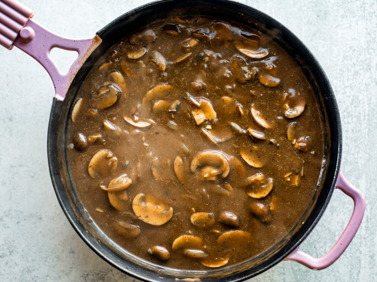 Skillet full of onions, mushrooms, and thickening gravy.