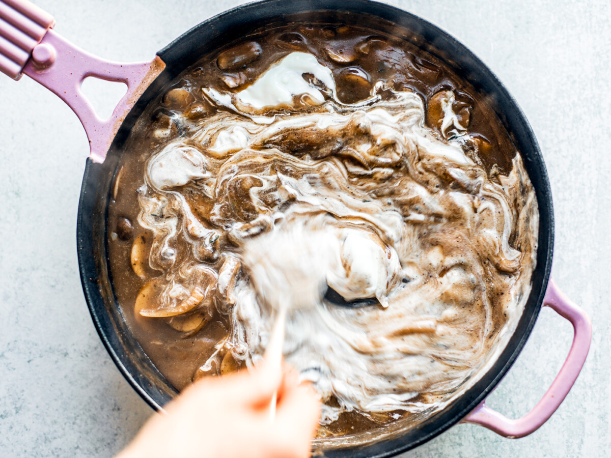 Sour cream being stirred into the gravy in the skillet.