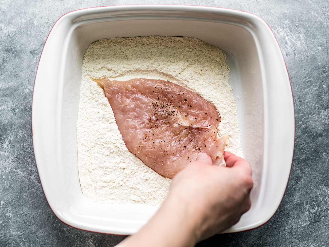 Hand dredging chicken cutlet in flour.