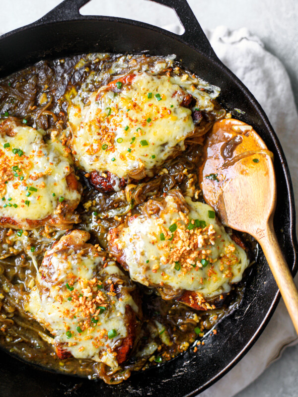 Cheesy pork chops smothered in onion gravy and topped with chives in a cast iron skillet with a wooden spoon.