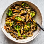 Bowl full of soba noodles and vegetables with a fork.