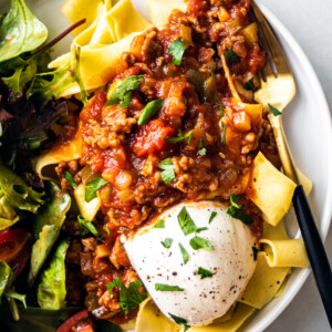 Close up shot of pappardelle pasta topped with meat sauce and burrata.