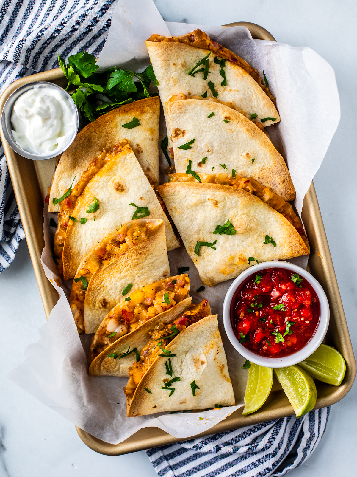 Shrimp quesadillas on a sheet pan with dipping bowls of sour cream and salsa.