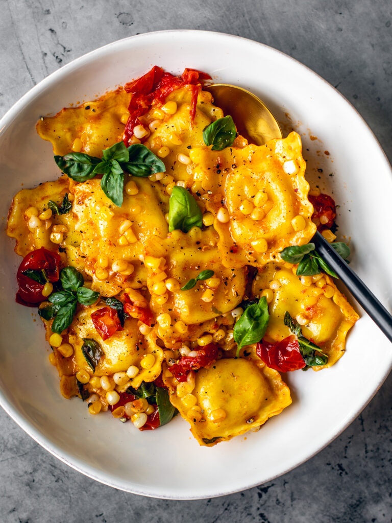 White bowl of cheese ravioli in lemon sauce with veggies.