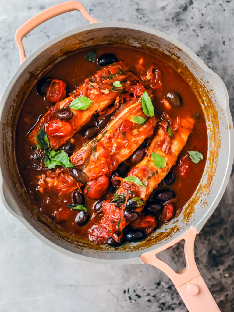 Sauté pan with salmon fillets in tomato and red wine sauce garnished with fresh basil.