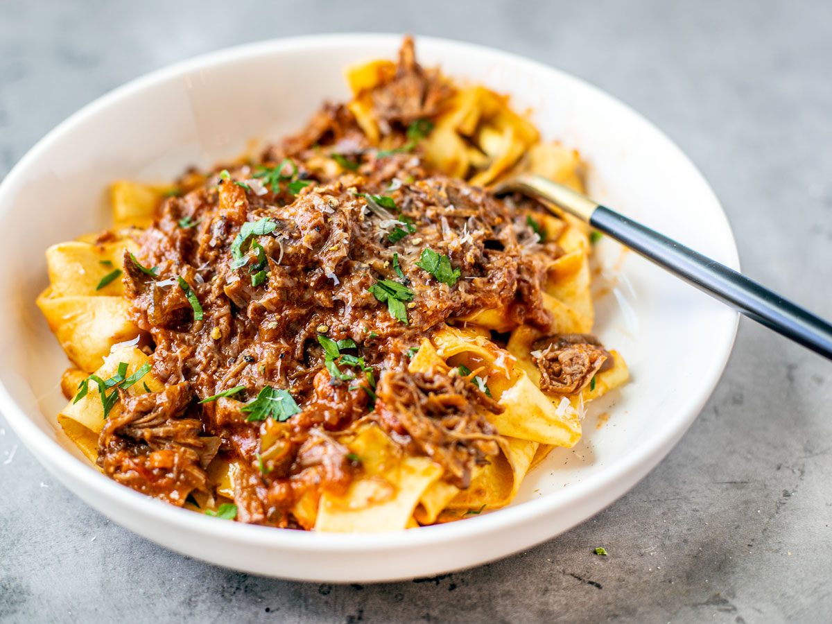 Serving bowl os pappardelle topped with pork ragu.