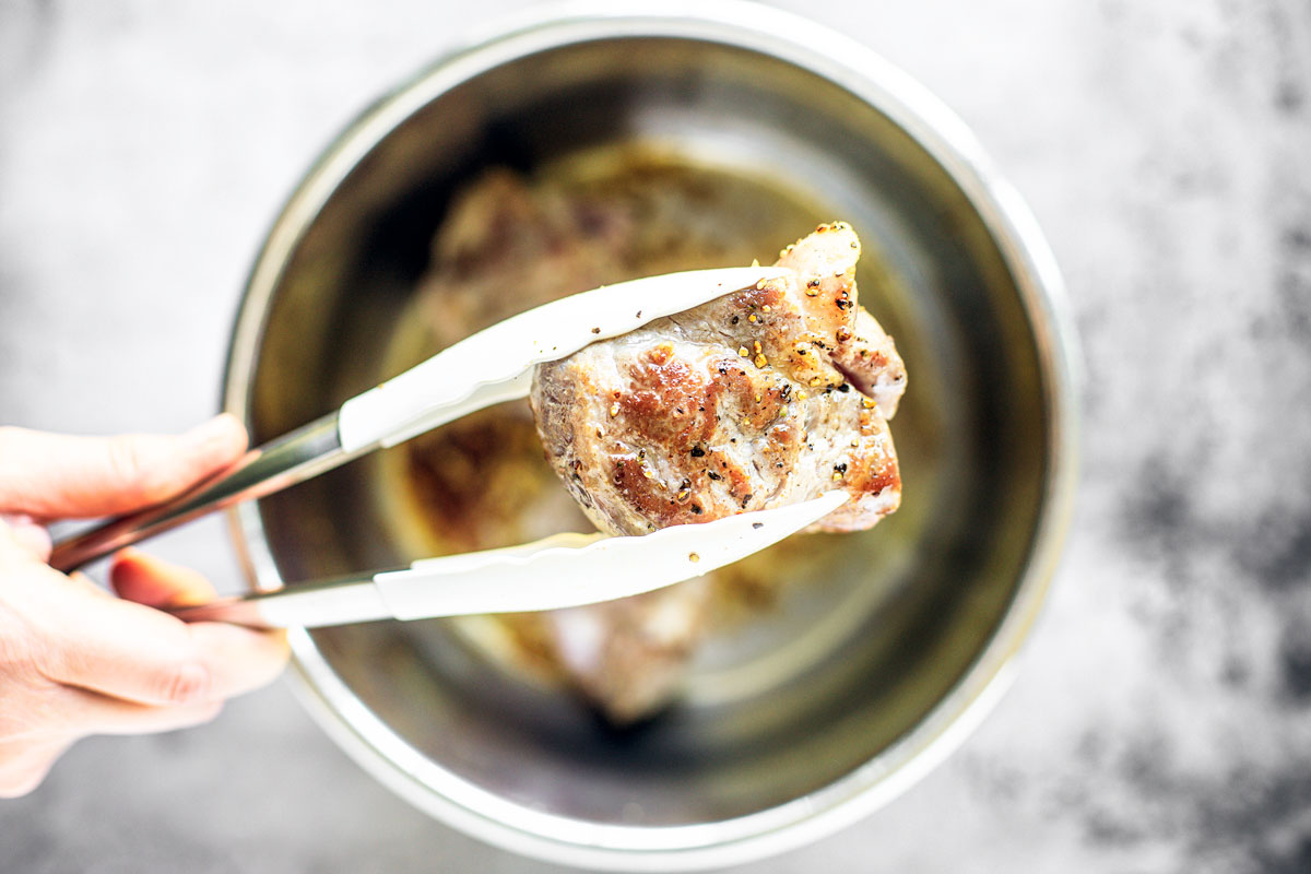 Tongs holding up eared browned pork.