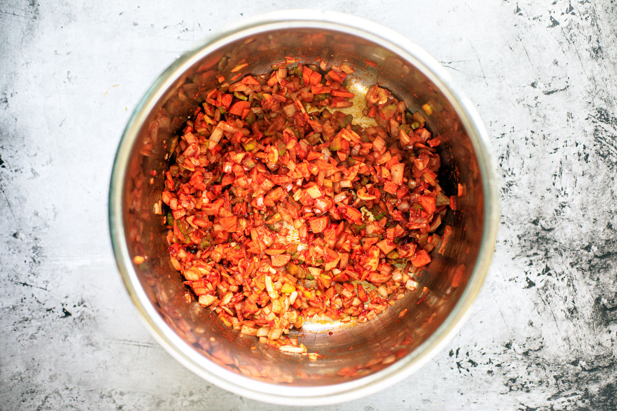 Instant Pot full of carrots, onions, and celery tossed in tomato paste.