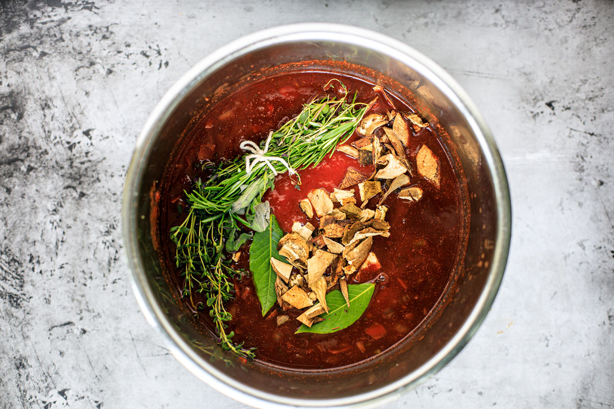 Instant Pot with sauce, before being cooked, with tied up fresh herbs and mushrooms.