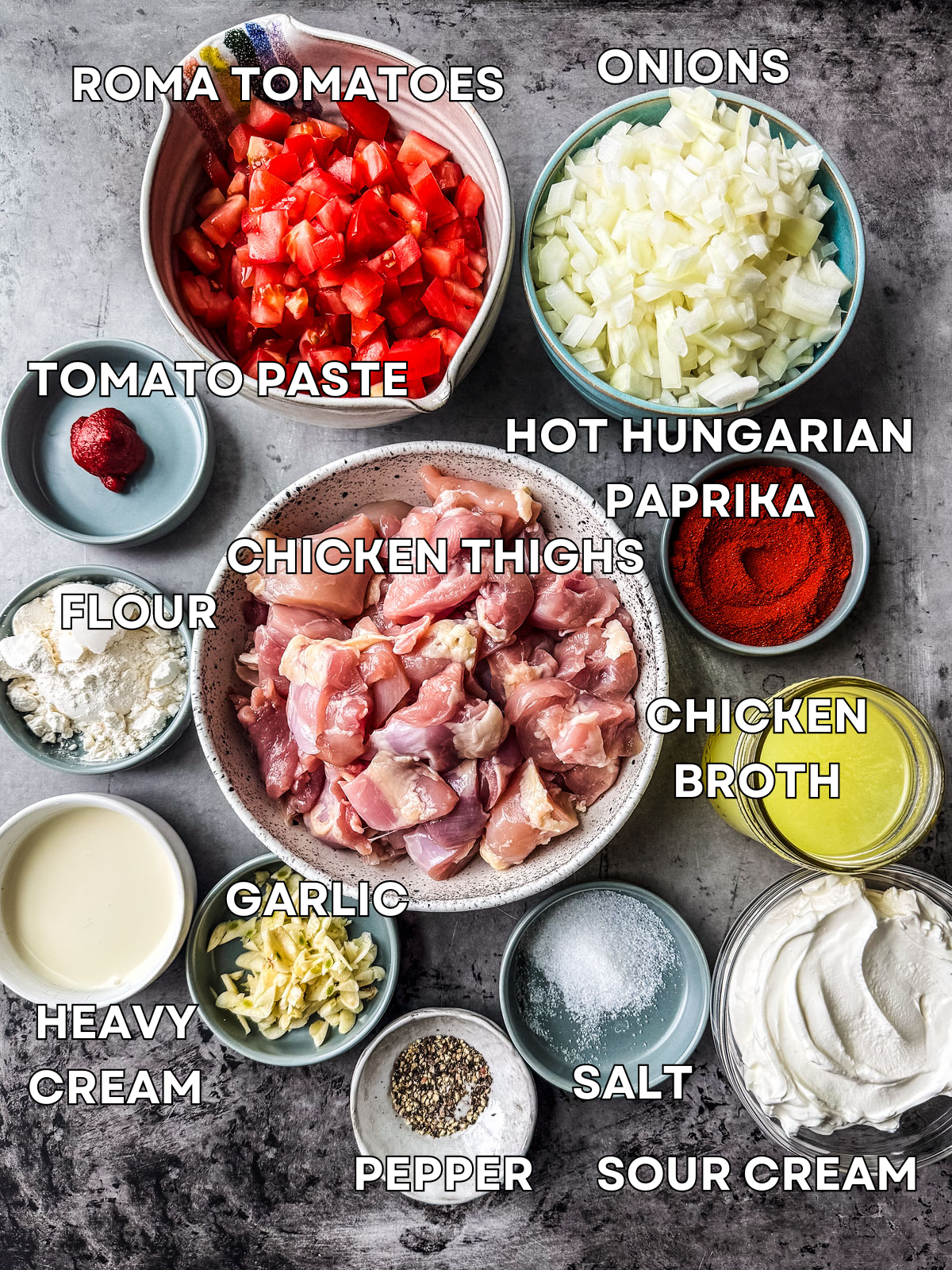 Ingredients for chicken paprikash laid out on a dark grey background.