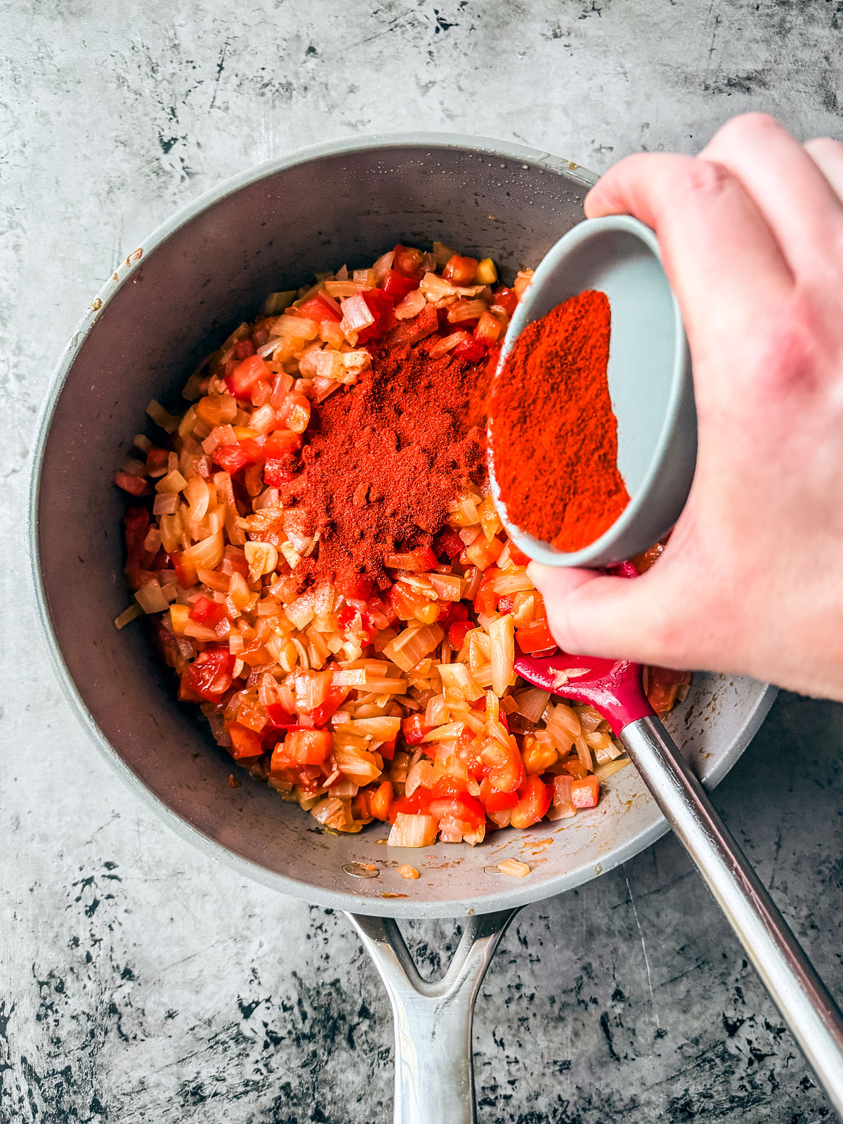 Paprika being added to the veggies in the pan.