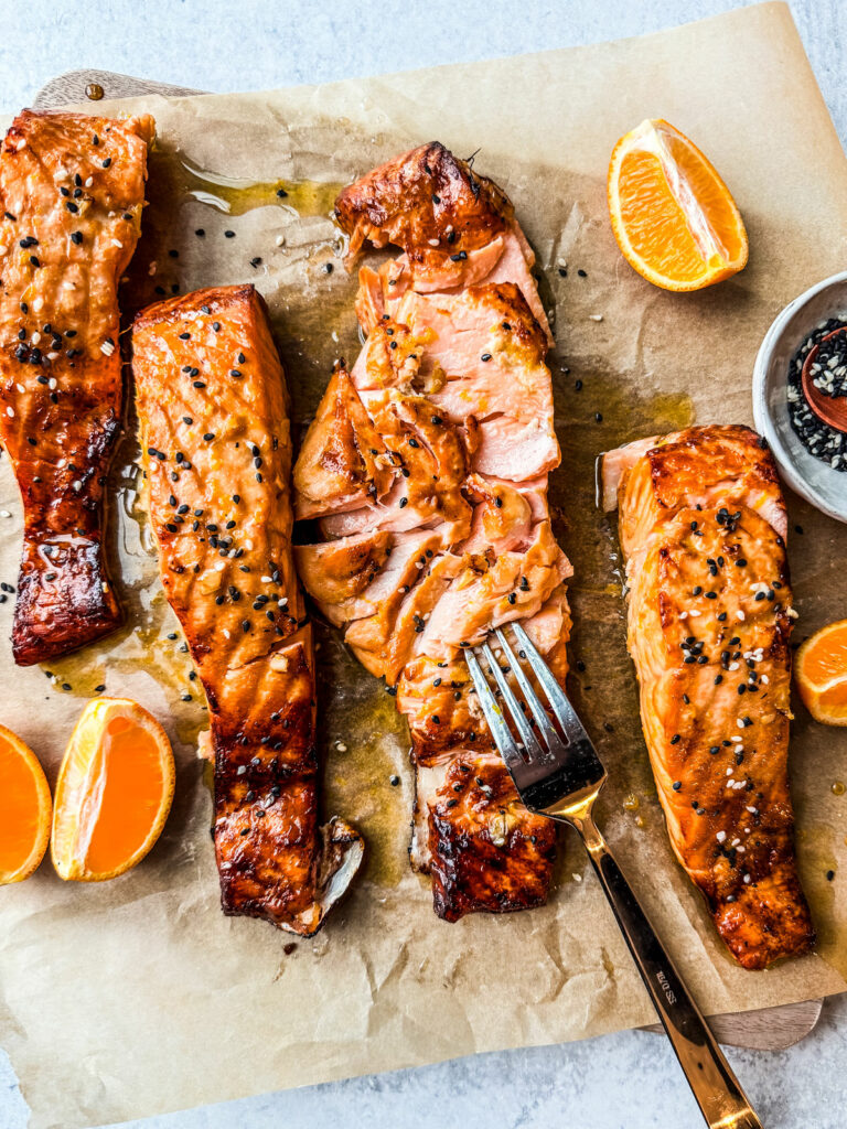 Salmon fillets on parchment, one flaked with a fork.