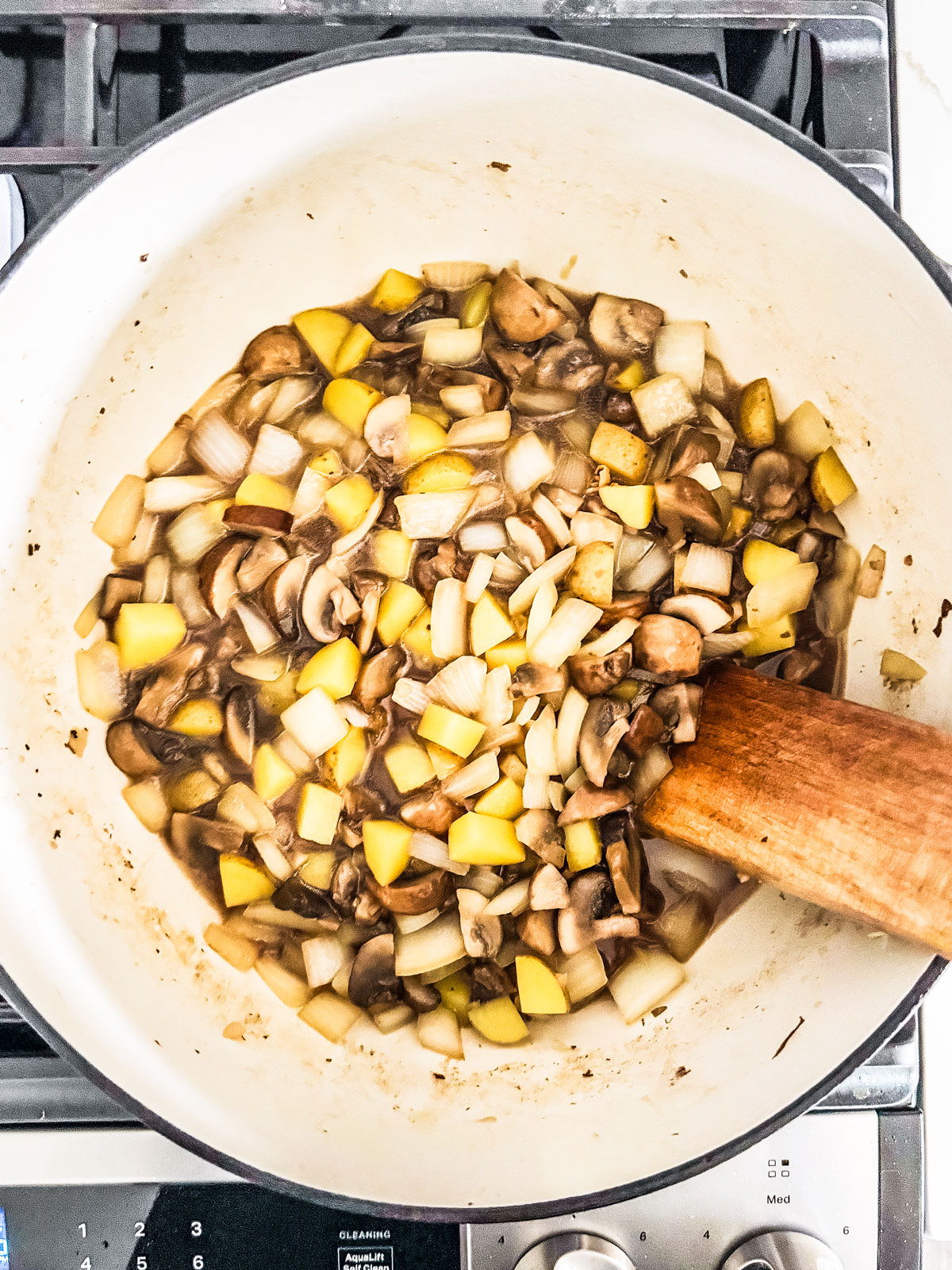 Pot full of cooked down onions, potatoes, and mushrooms.