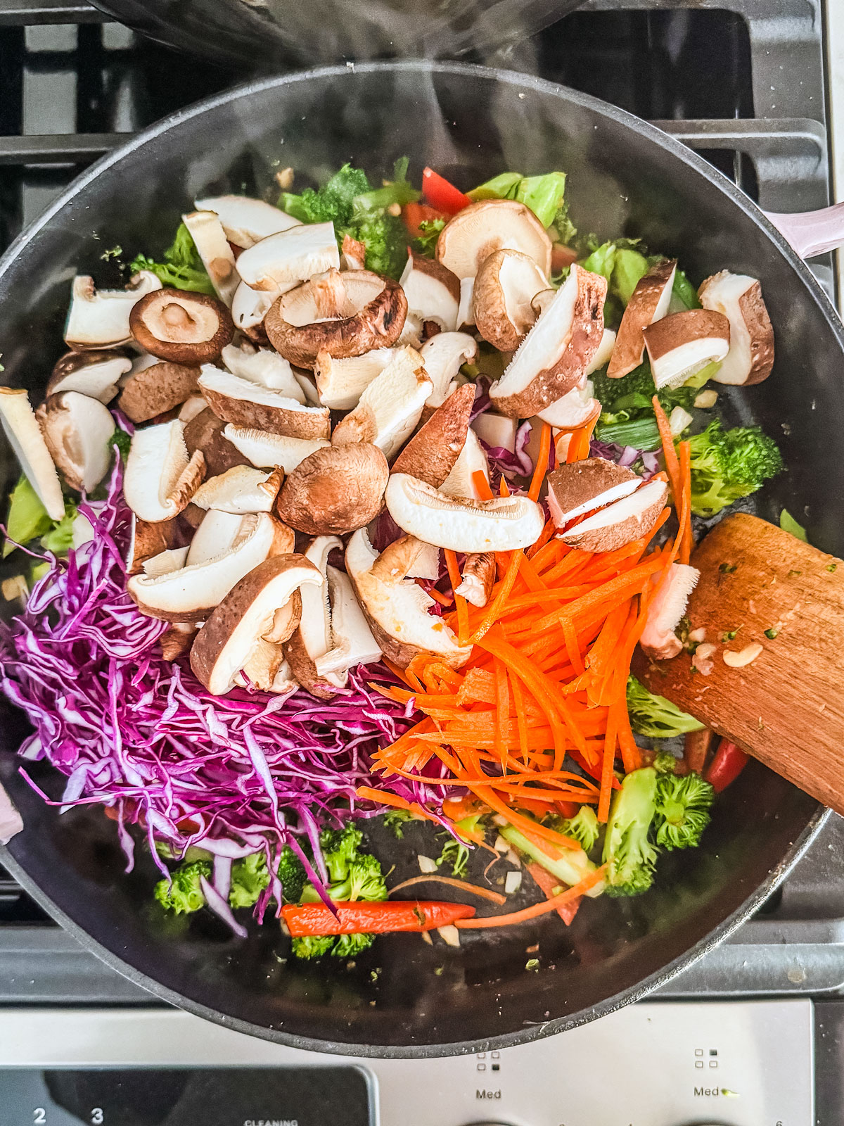 A variety of veggies in a cast iron pan being stirred.