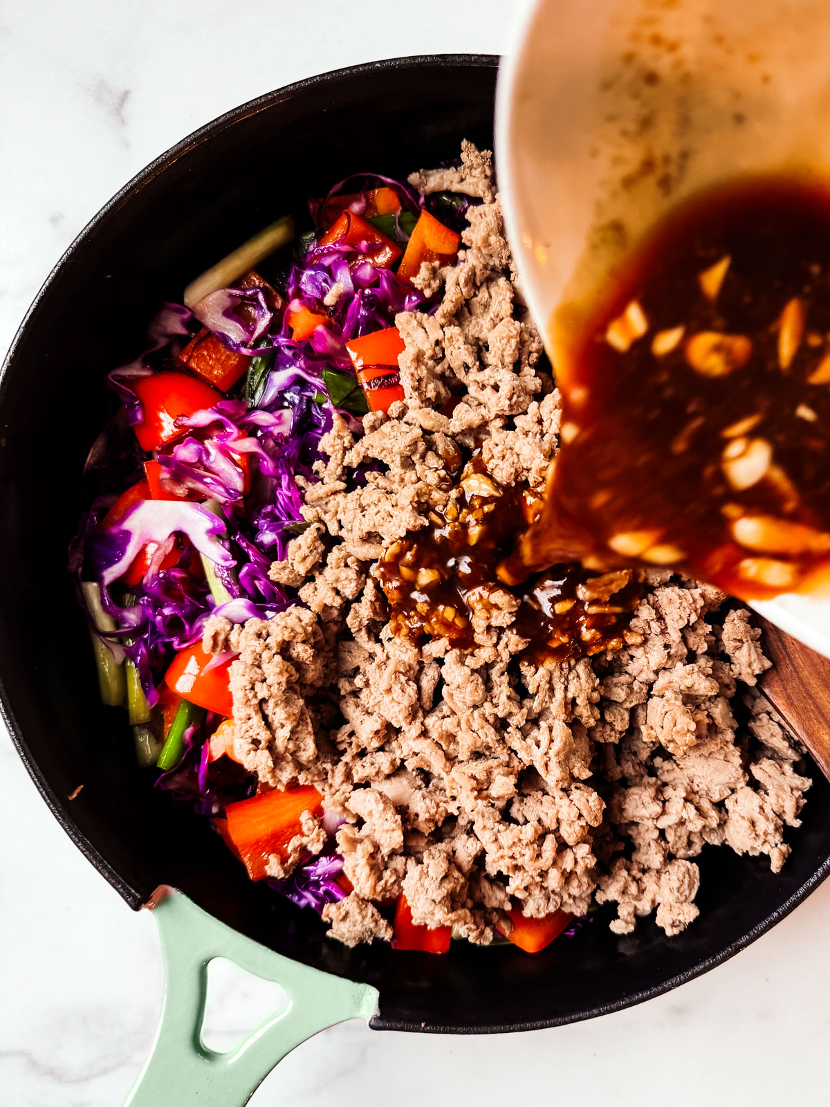 Ground turkey and vegetables in a skillet with sauce being poured over it.