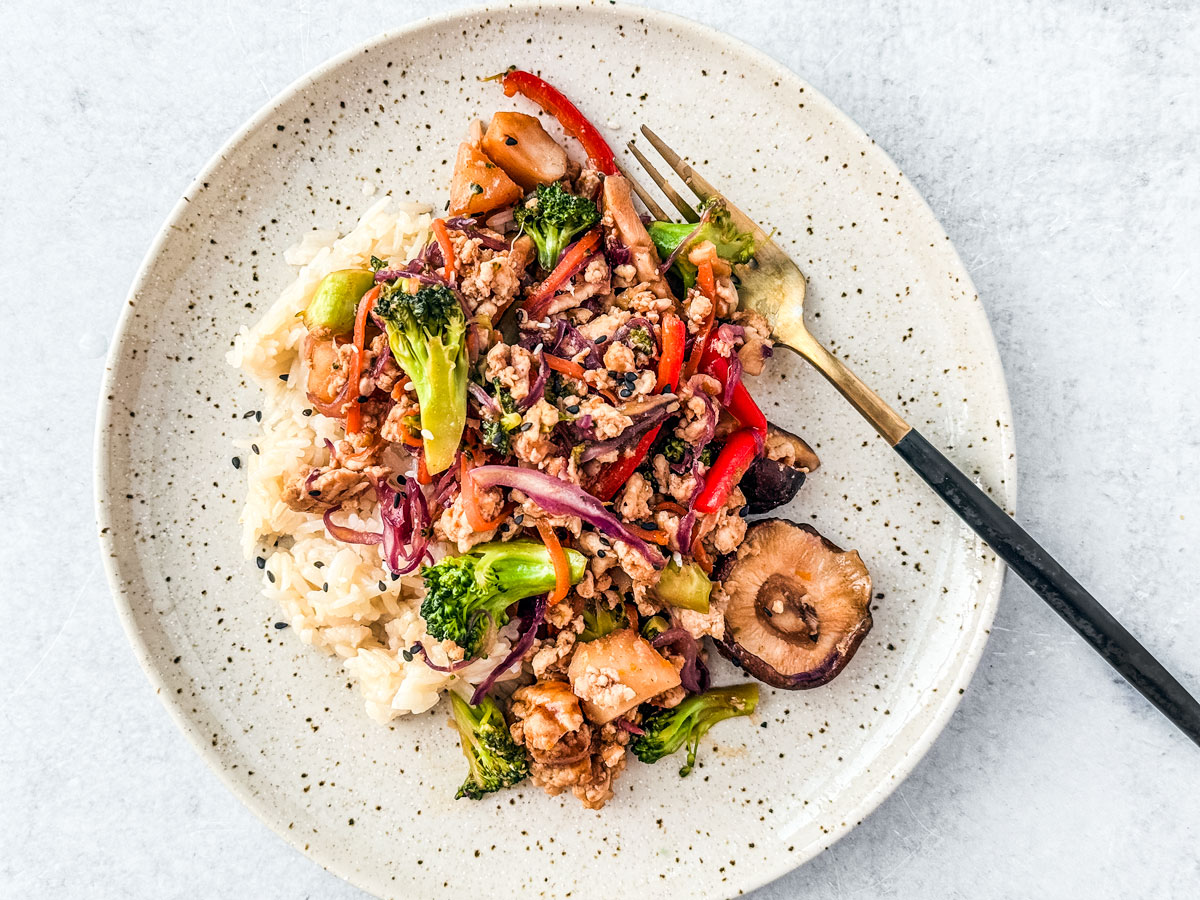 A plate of rice with ground turkey stir fry with cabbage served on top of it.