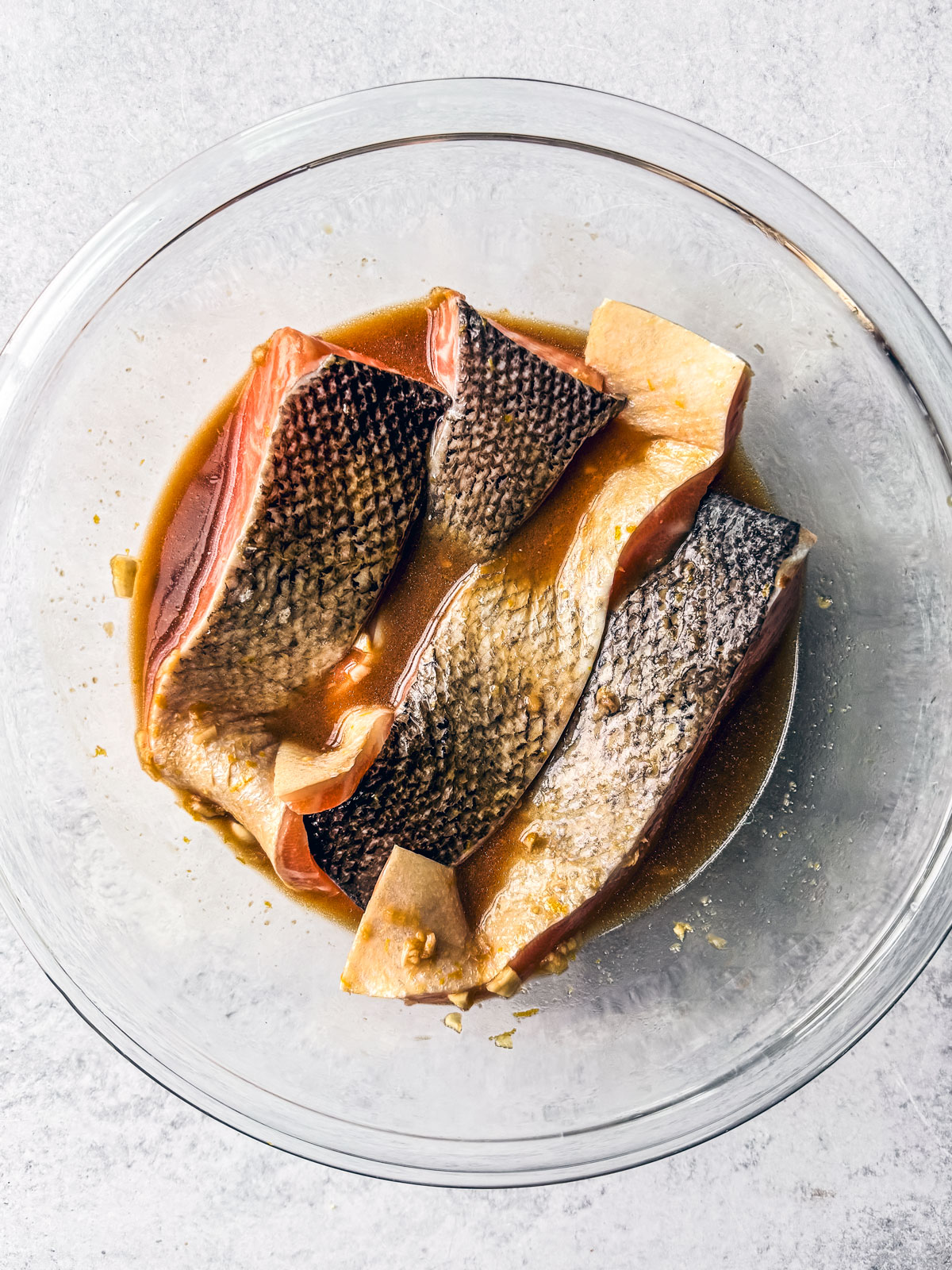 Salmon fillets marinating in a glass bowl.