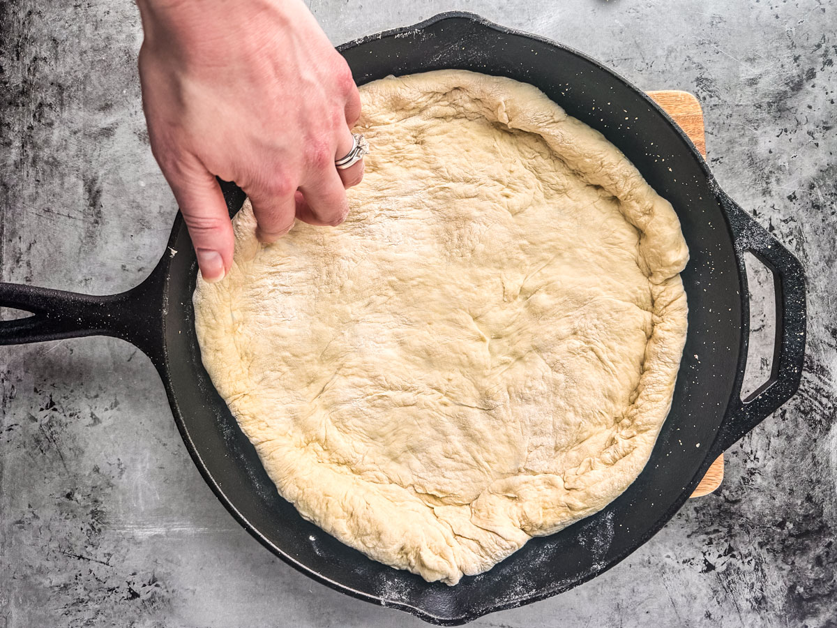 Dough being fit into the cast iron skillet.