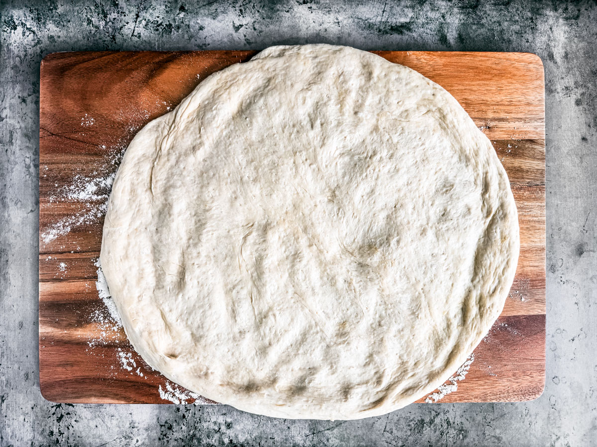 Raw dough worked into a circle on a wooden board.