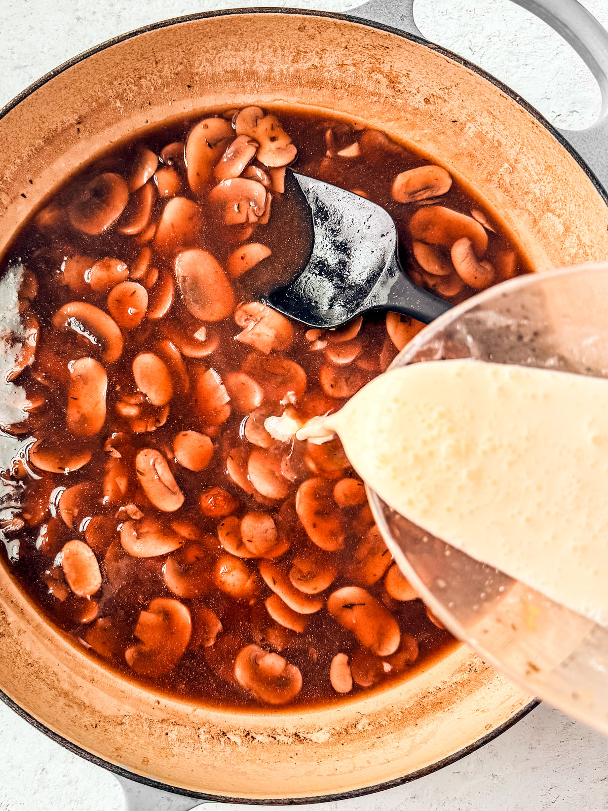 Cream being added to the pan with mushrooms and liquid.