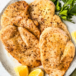 Plate of cooked chicken cutlets with lemon wedges and parsley.