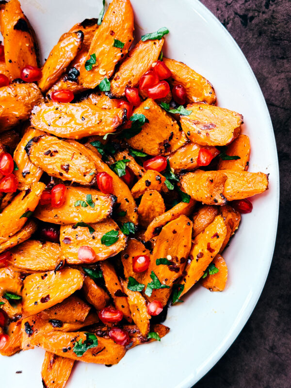 hot honey roasted carrots garnished with pomegranate arils and parsley.