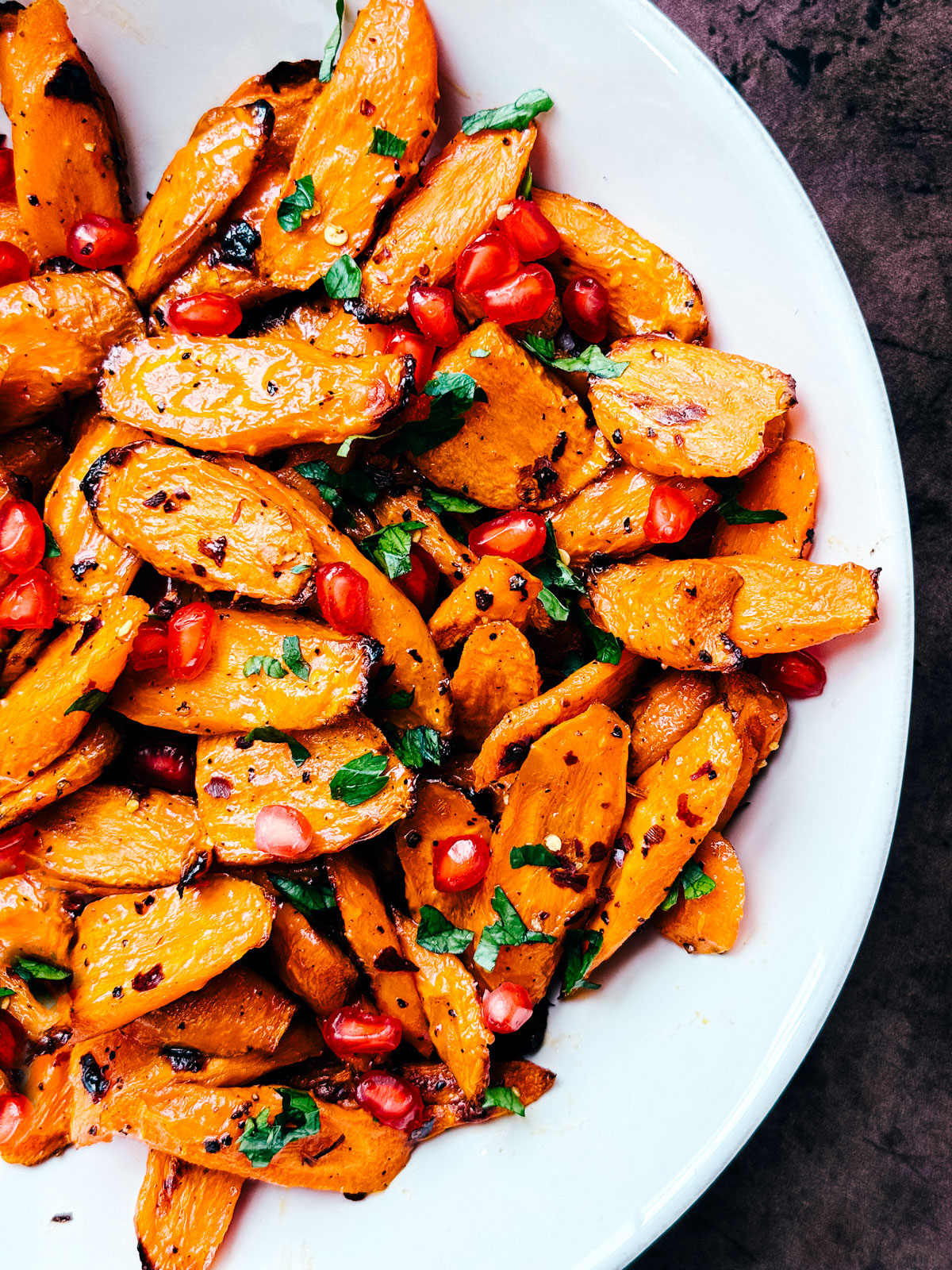 Serving bowl of hot honey roasted carrots garnished with pomegranate arils and parsley.