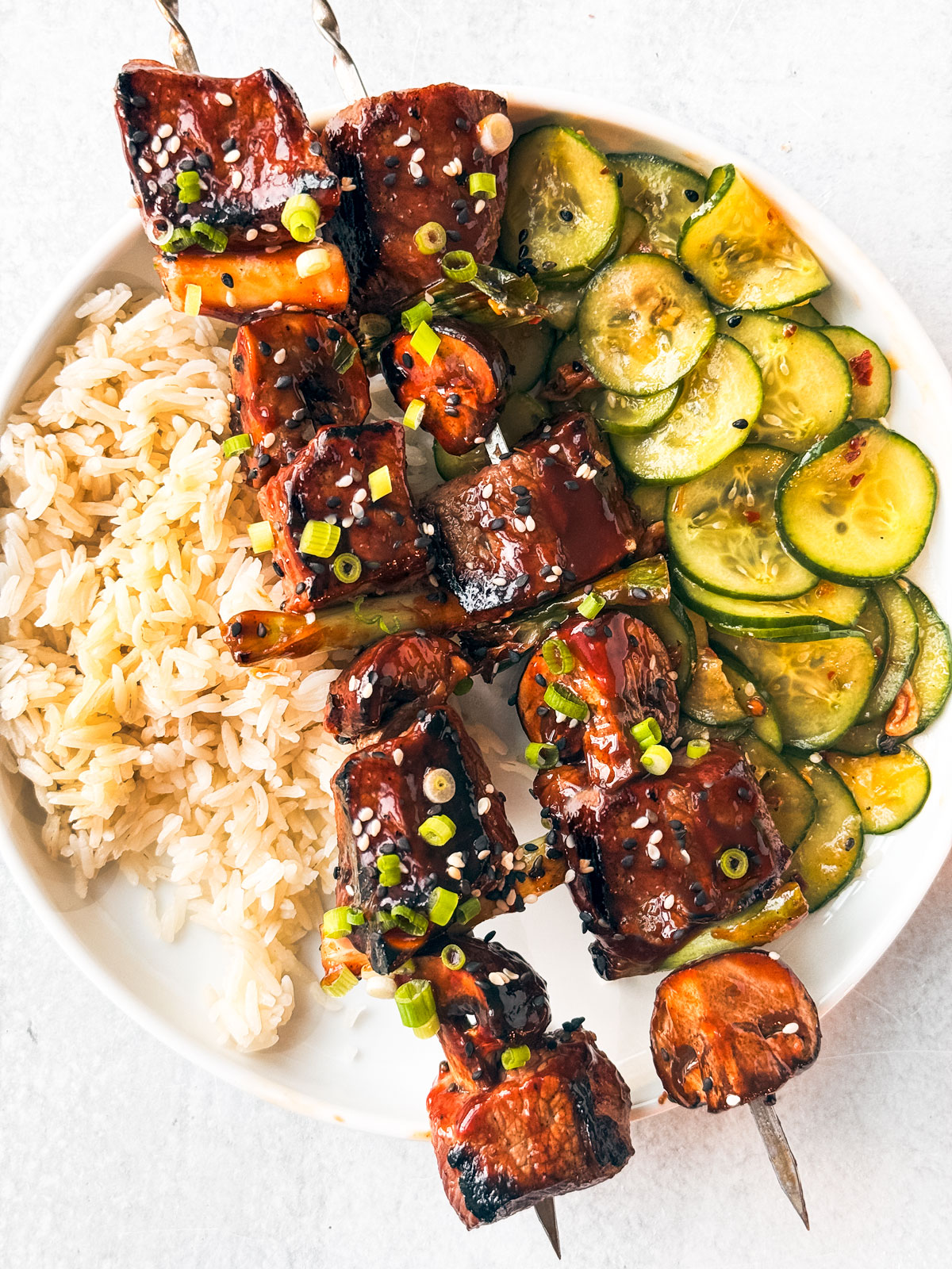 Plate of rice, cucumber salad, and saucy Korean BBQ beef skewers.