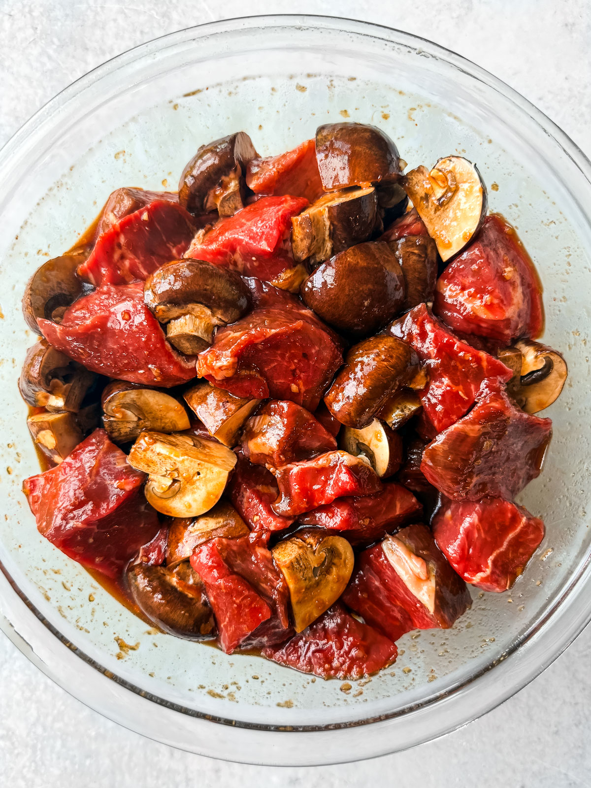 Beef chunks and mushrooms in a mixing bowl marinating.