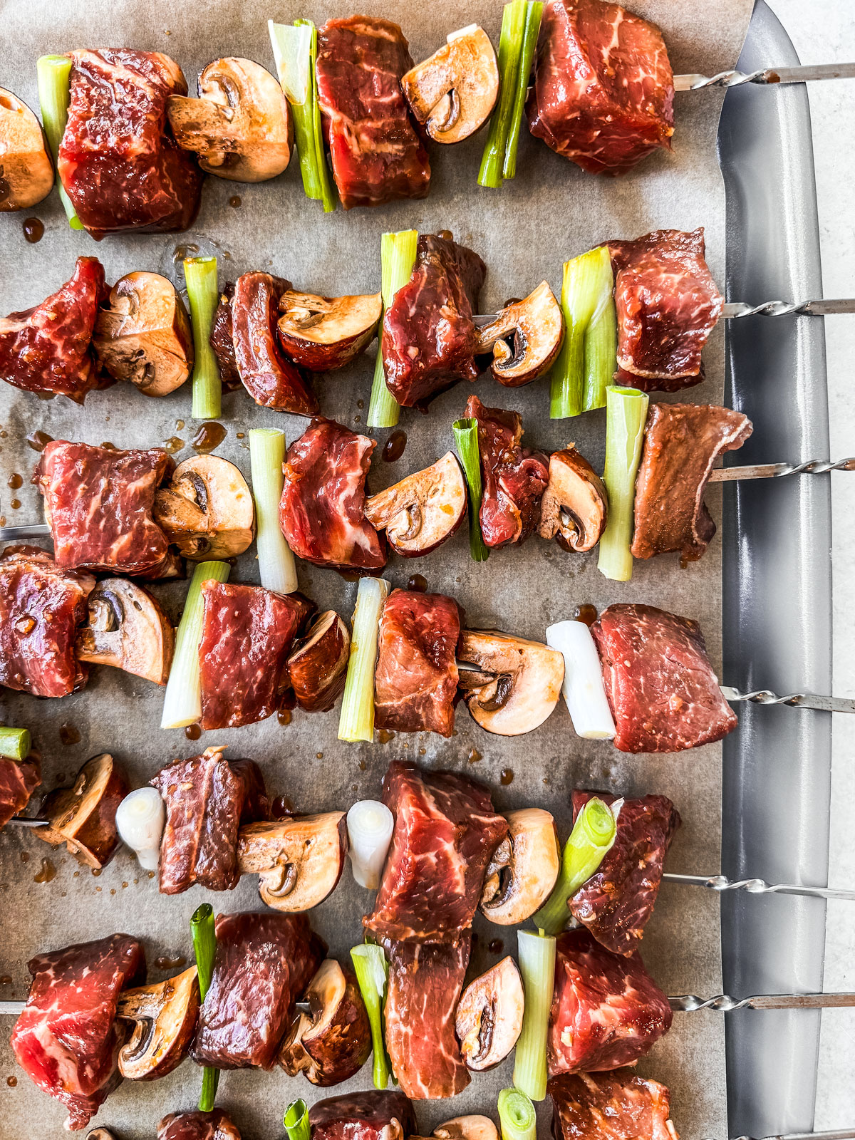 Uncooked beef, mushrooms, and scallions threaded onto metal skewers.
