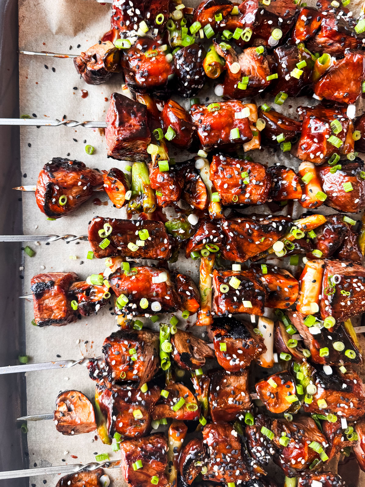 Saucy beef skewers on a baking sheet garnished with chopped scallions.