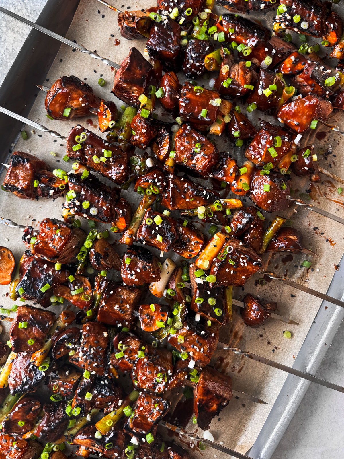 Beef skewers piled onto a baking sheet topped with chopped scallions.﻿